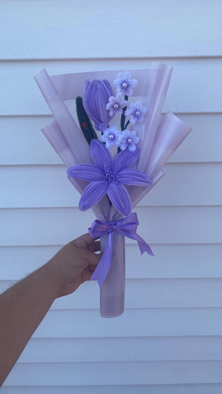 Purple artificial flower bouquet wrapped in purple cellophane and tied with a ribbon.