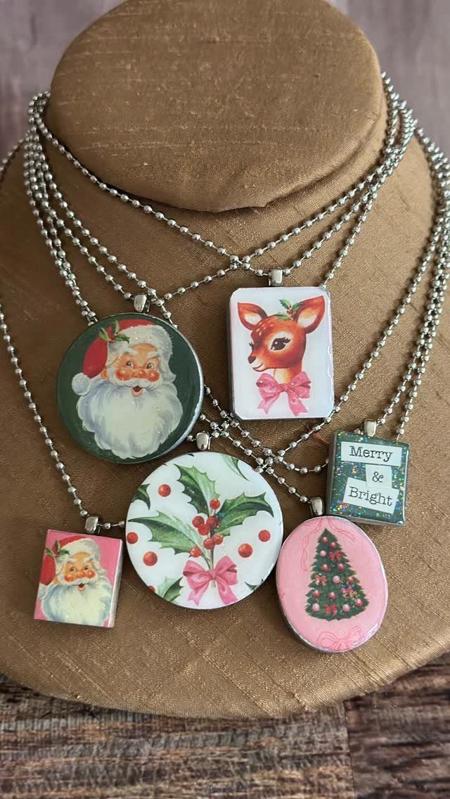 Christmas-themed necklaces with Santa and reindeer pendants displayed on a tan jewelry bust.
