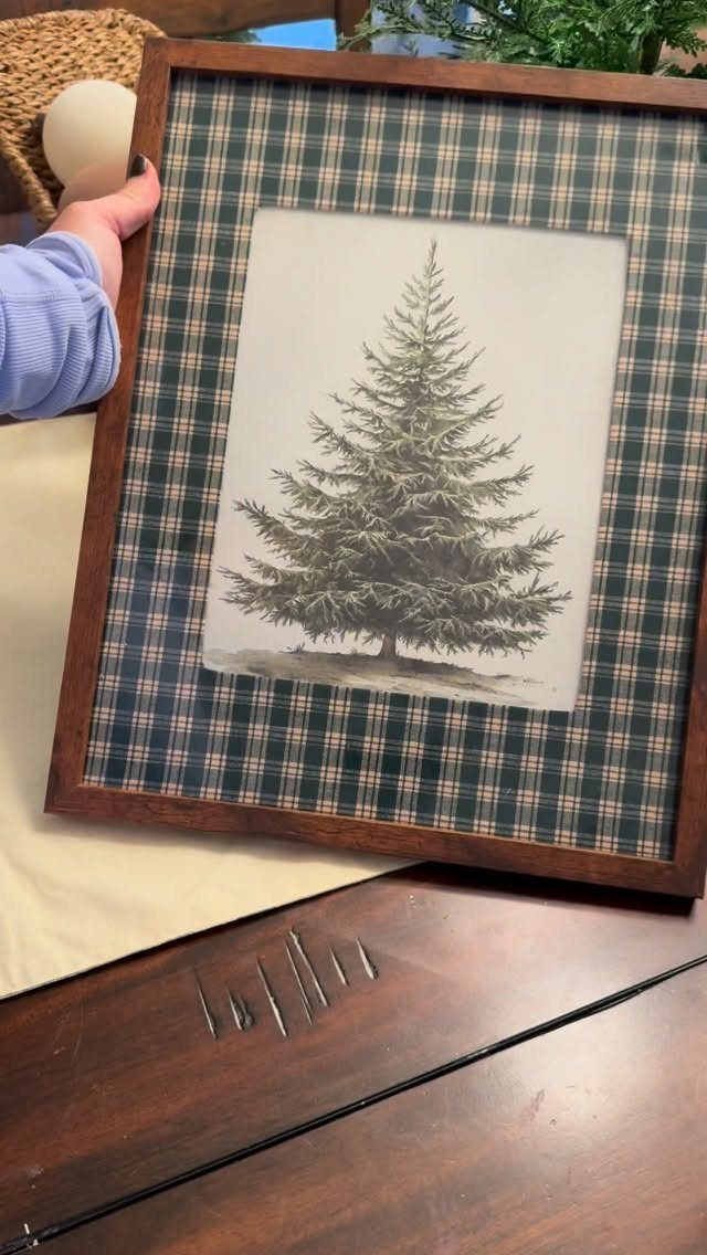 Wooden framed picture of a pine tree with a plaid fabric matting.