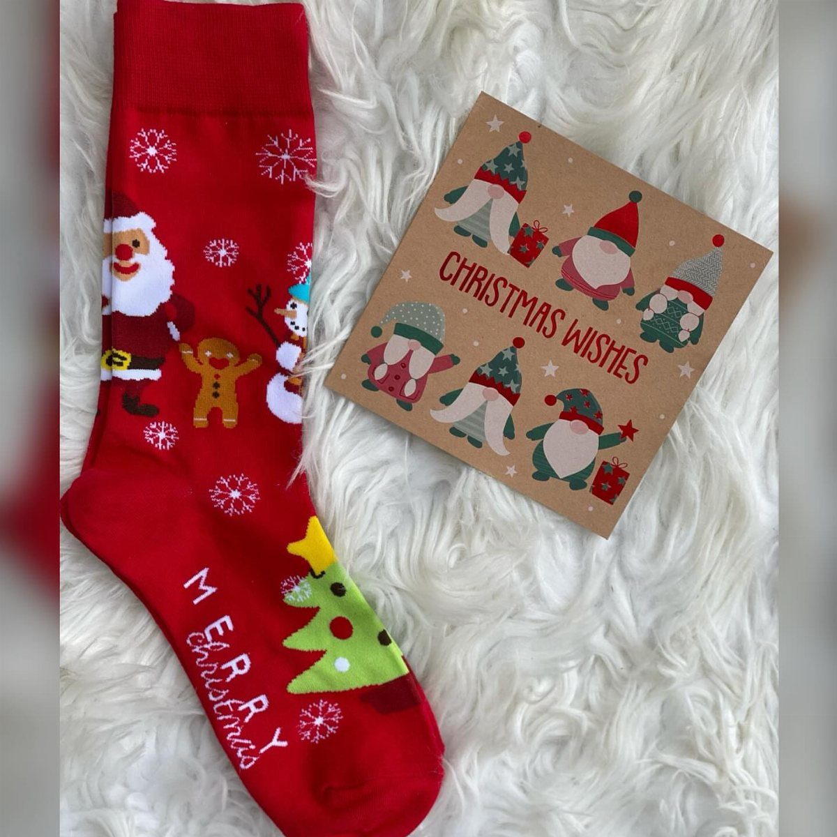 Red Christmas sock and a gnome greeting card on white faux-fur background.