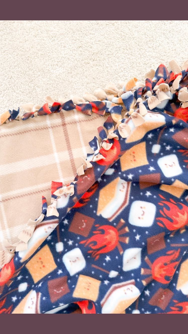 Fleece tie blanket with campfire patterns and beige plaid joined by knotted edges.