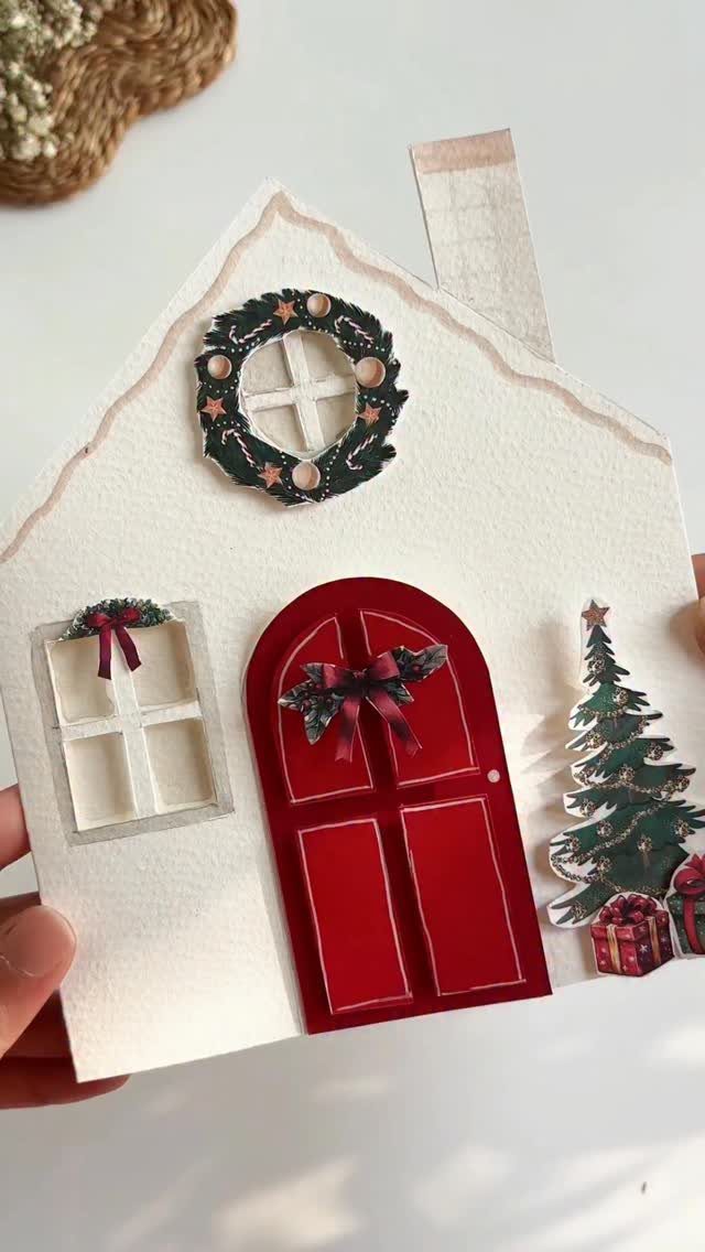 Handmade house-shaped Christmas card with a red door and festive decorations.