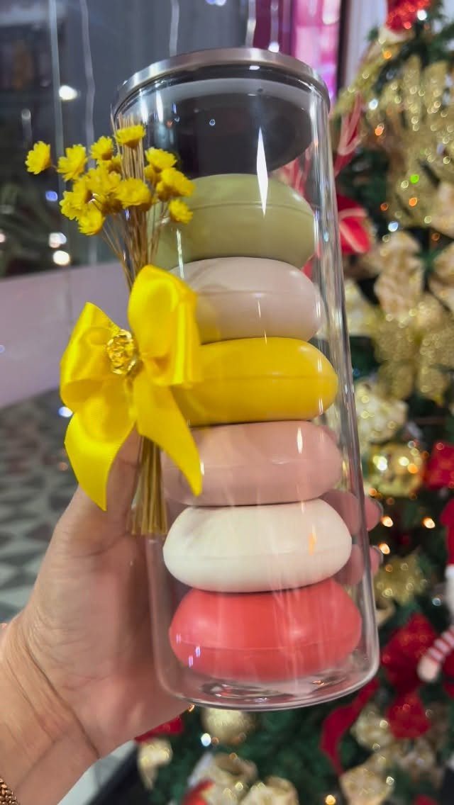 Stacked colorful oval soaps in a clear cylinder with a yellow ribbon bow.