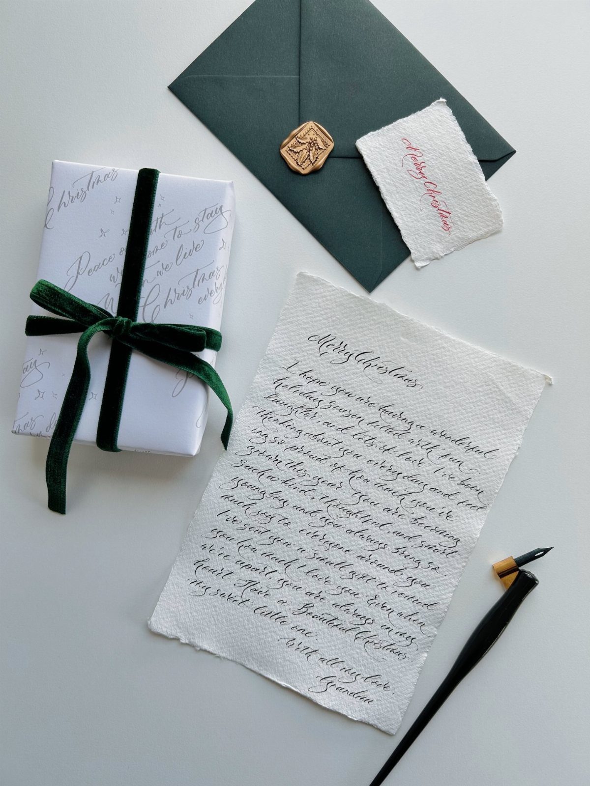 Handwritten calligraphy letter with a dark green envelope and a wrapped gift.