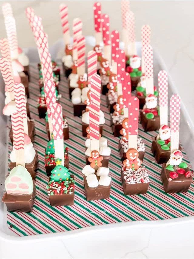 Chocolate treats on striped sticks decorated with miniature Christmas figures on a tray.
