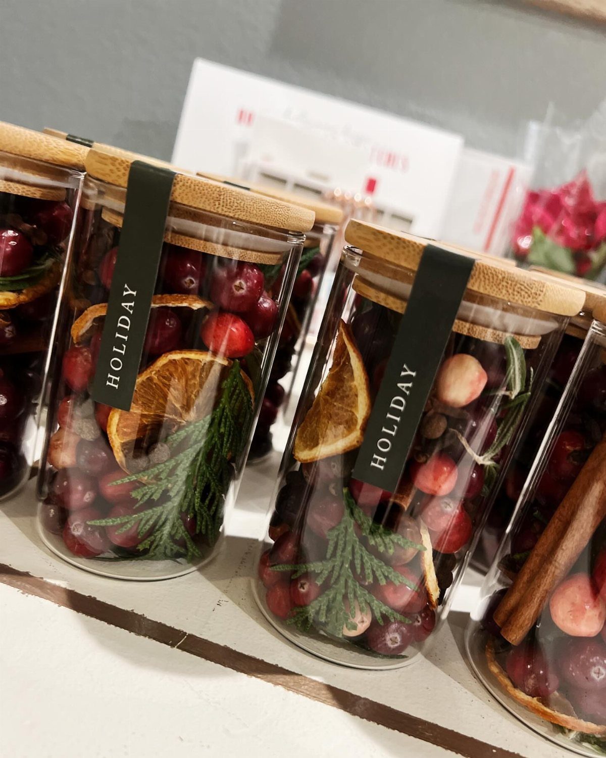 Glass jars with bamboo lids filled with cranberries, orange slices, and pine needles.