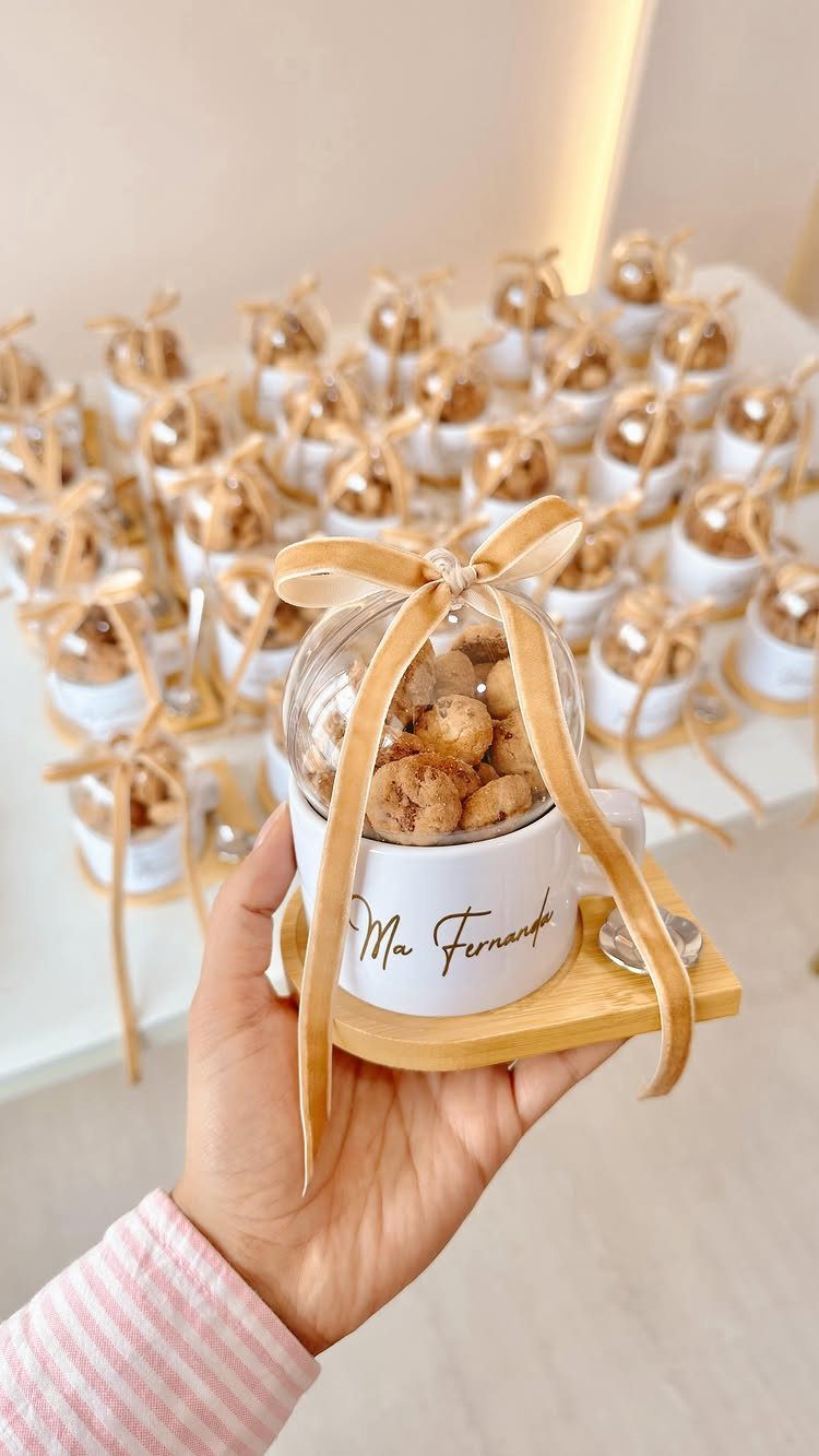Personalized white mug filled with cookies, topped with a gold ribbon bow.