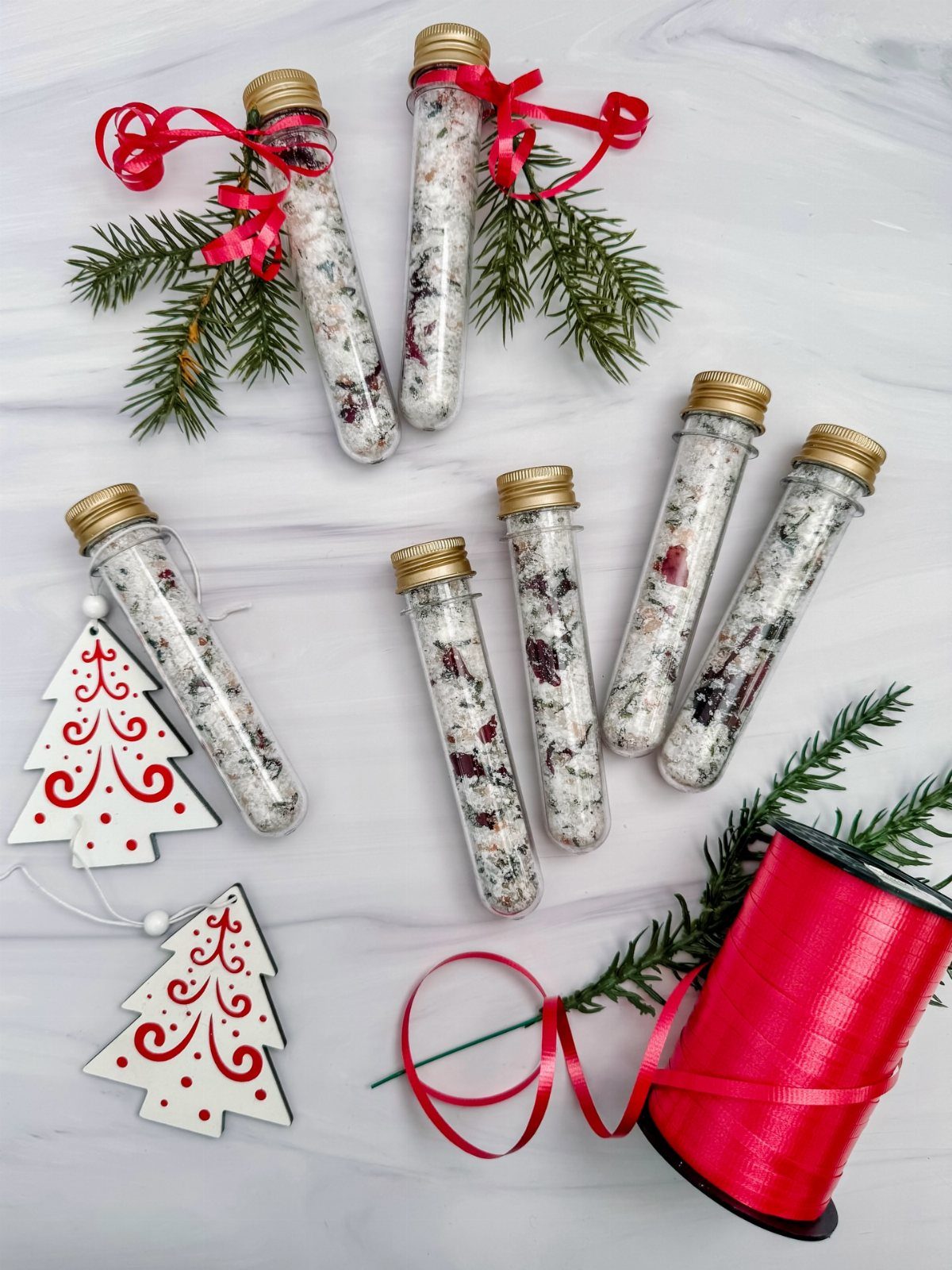 Glass test tubes filled with bath salts surrounded by pine branches and red ribbons.