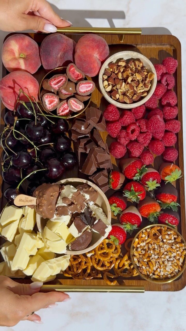 Chocolate charcuterie board with berries, nuts, pretzels, and various chocolates on a wooden tray.