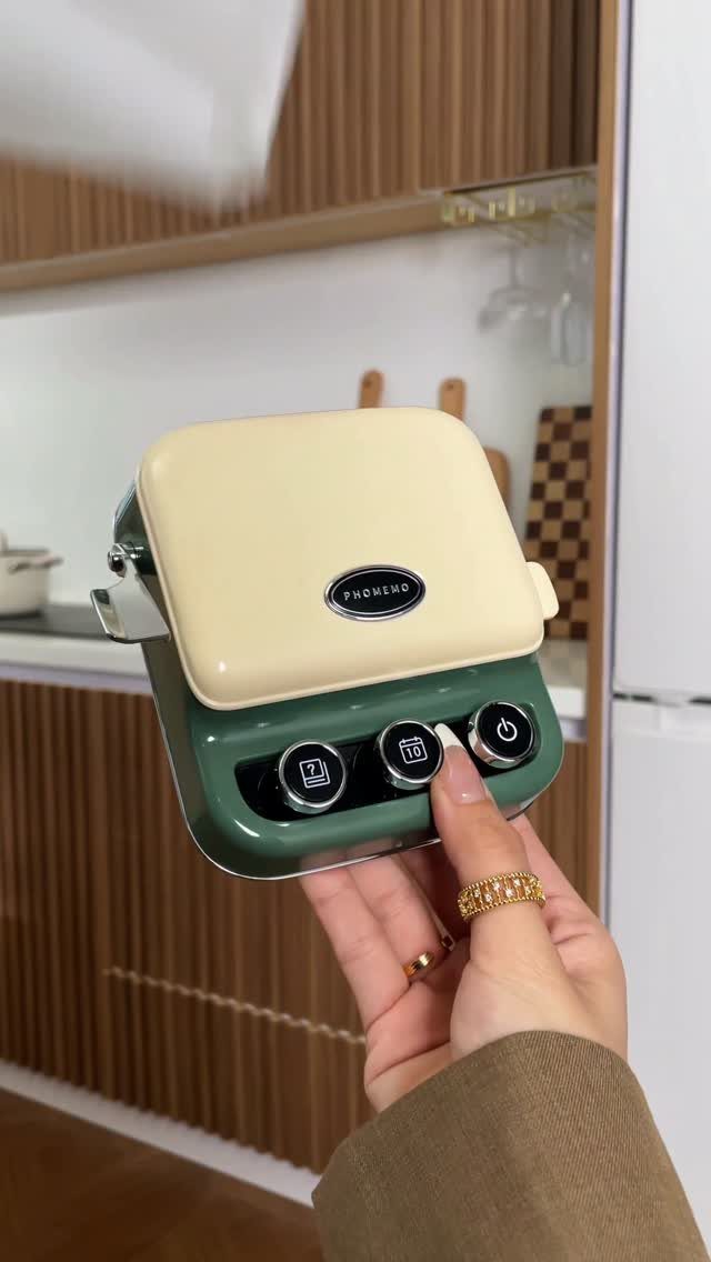 Small cream and green sandwich maker held by a hand in a kitchen.