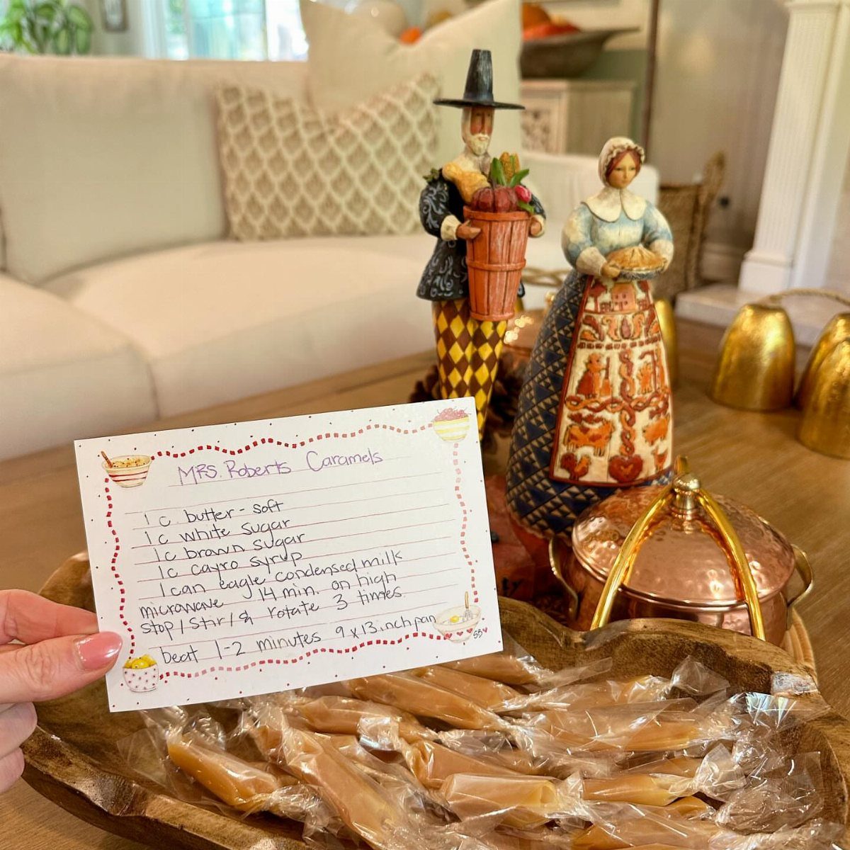 Handwritten recipe card for caramels held over a tray of wrapped homemade candies.