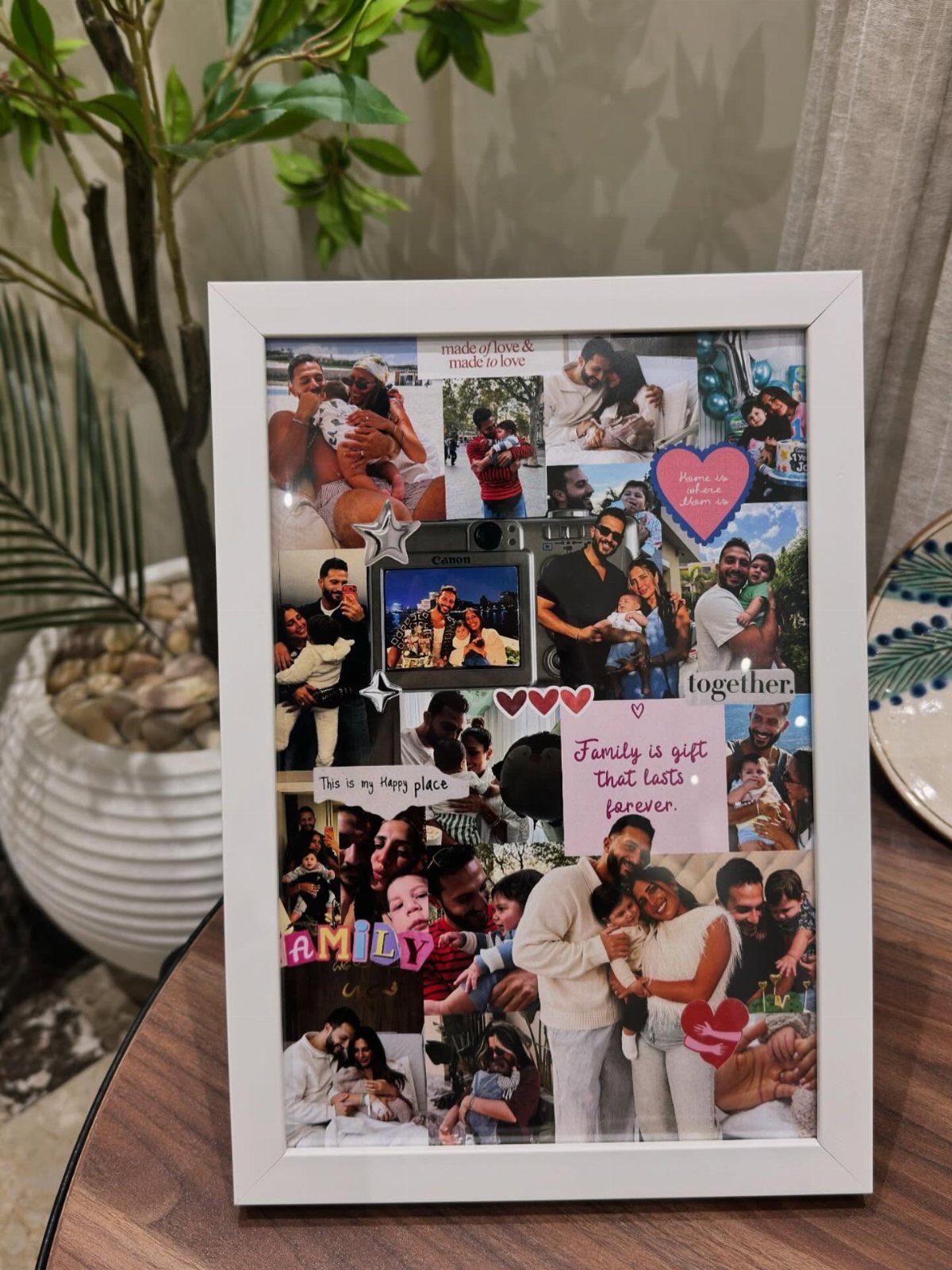 White framed collage of family photos with heart decorations on a wooden table.
