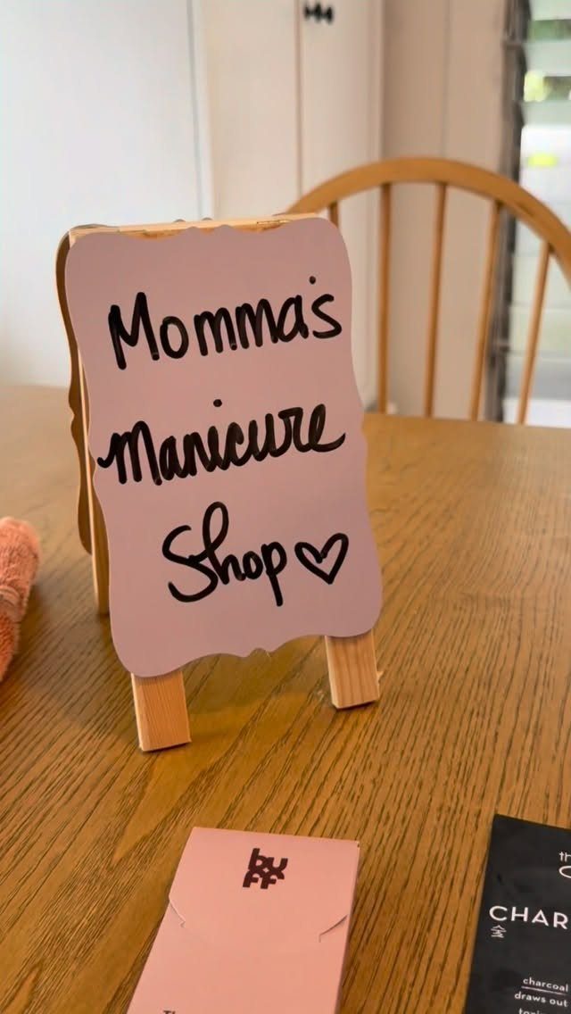 Handmade pink sign on a wooden easel reading Momma's Manicure Shop on a table