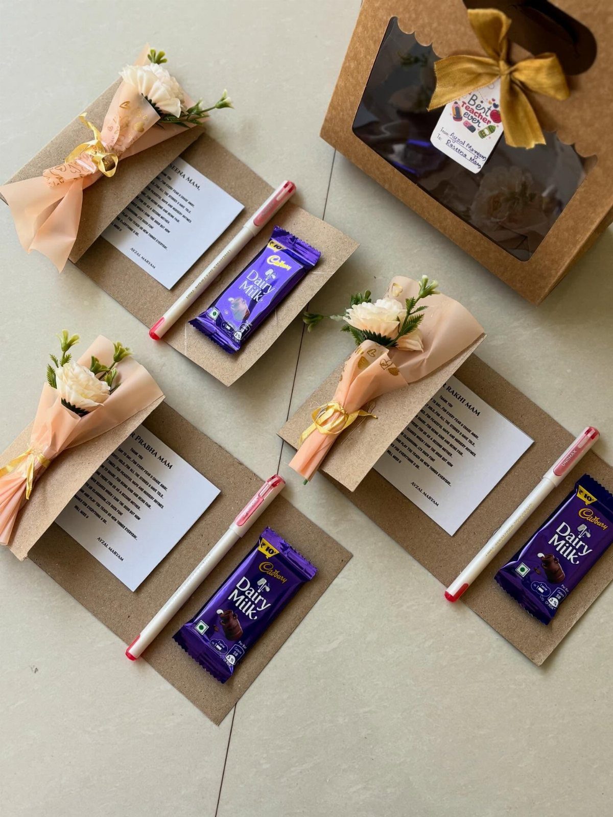 Three gift sets with purple chocolate bars, white pens, and small flower bouquets.