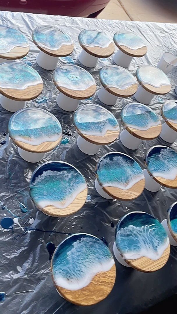 Wood slice coasters with blue resin ocean wave designs resting on white supports.
