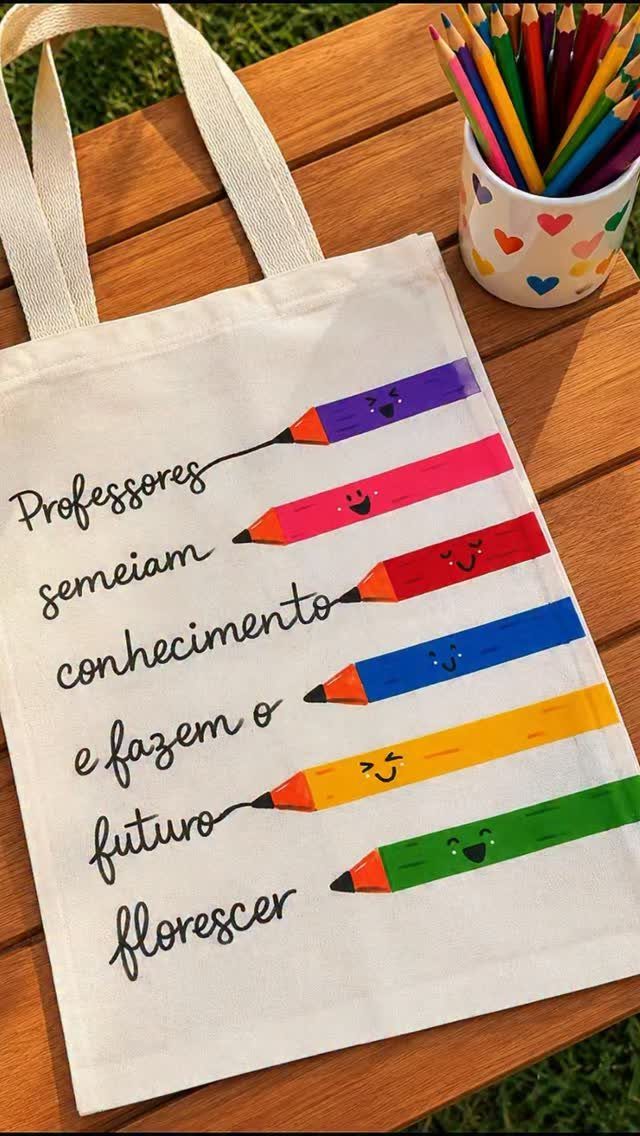 White canvas tote bag with colorful pencil illustrations and Portuguese text on wooden table