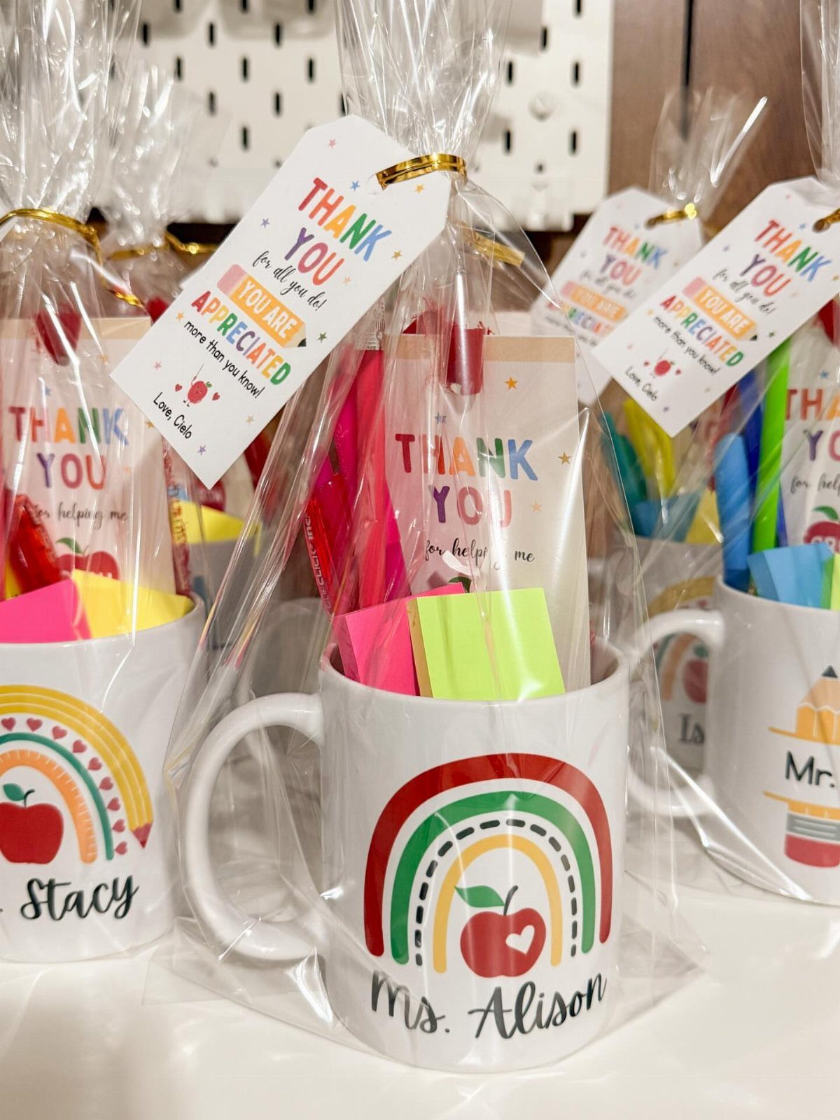 Teacher gift mugs wrapped in cellophane with rainbows, apples, and thank you notes.