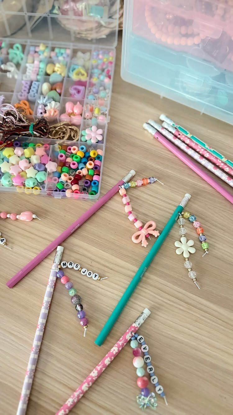 Colorful pencils with beaded charms and a box of multicolored beads on wood.