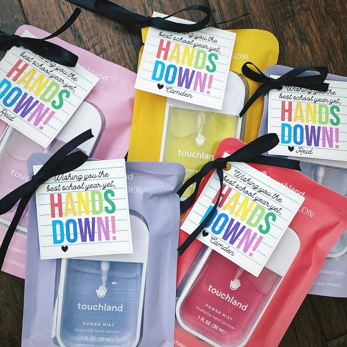Four colorful hand sanitizer sprays wrapped in fabric with personalized teacher gift tags.