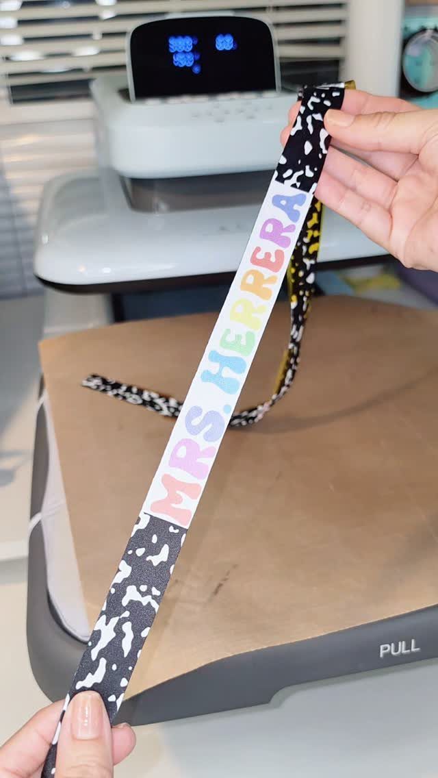 Personalized lanyard with animal print and colorful name held over a heat press.