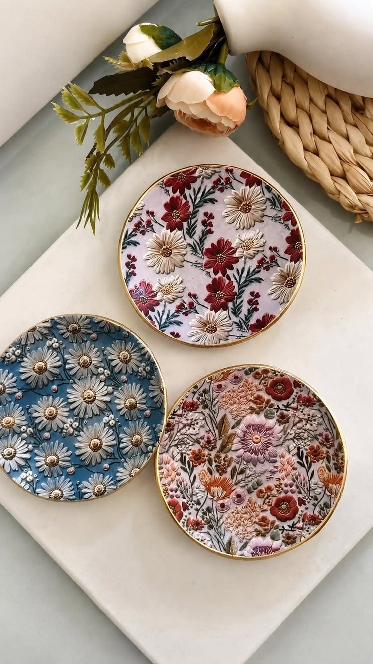 Three small floral patterned dishes with gold rims on a white surface.