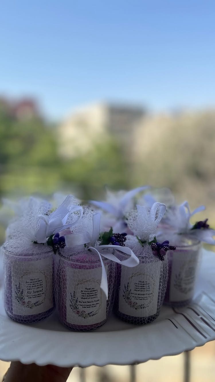 Purple scented candles in glass jars with white tulle bows on a white plate.
