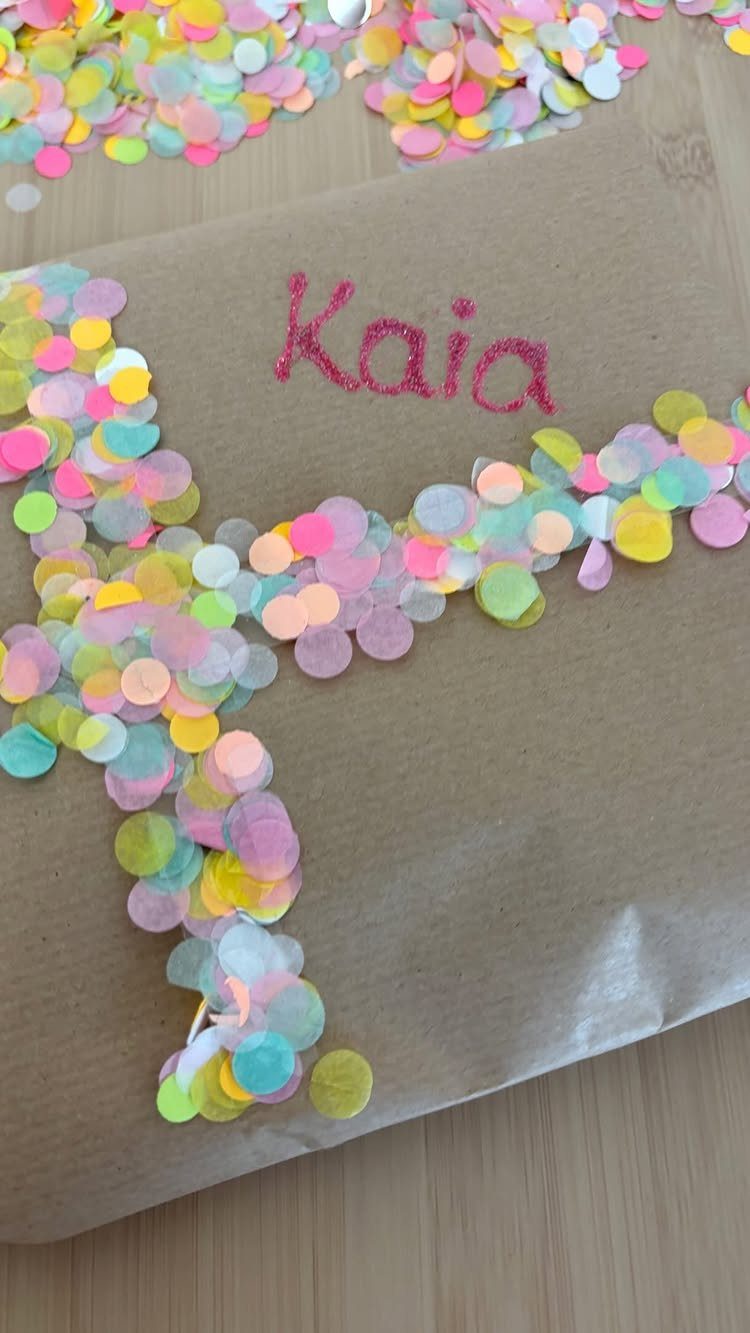 Brown kraft paper wrapped gift with red glitter text and pastel confetti circles.