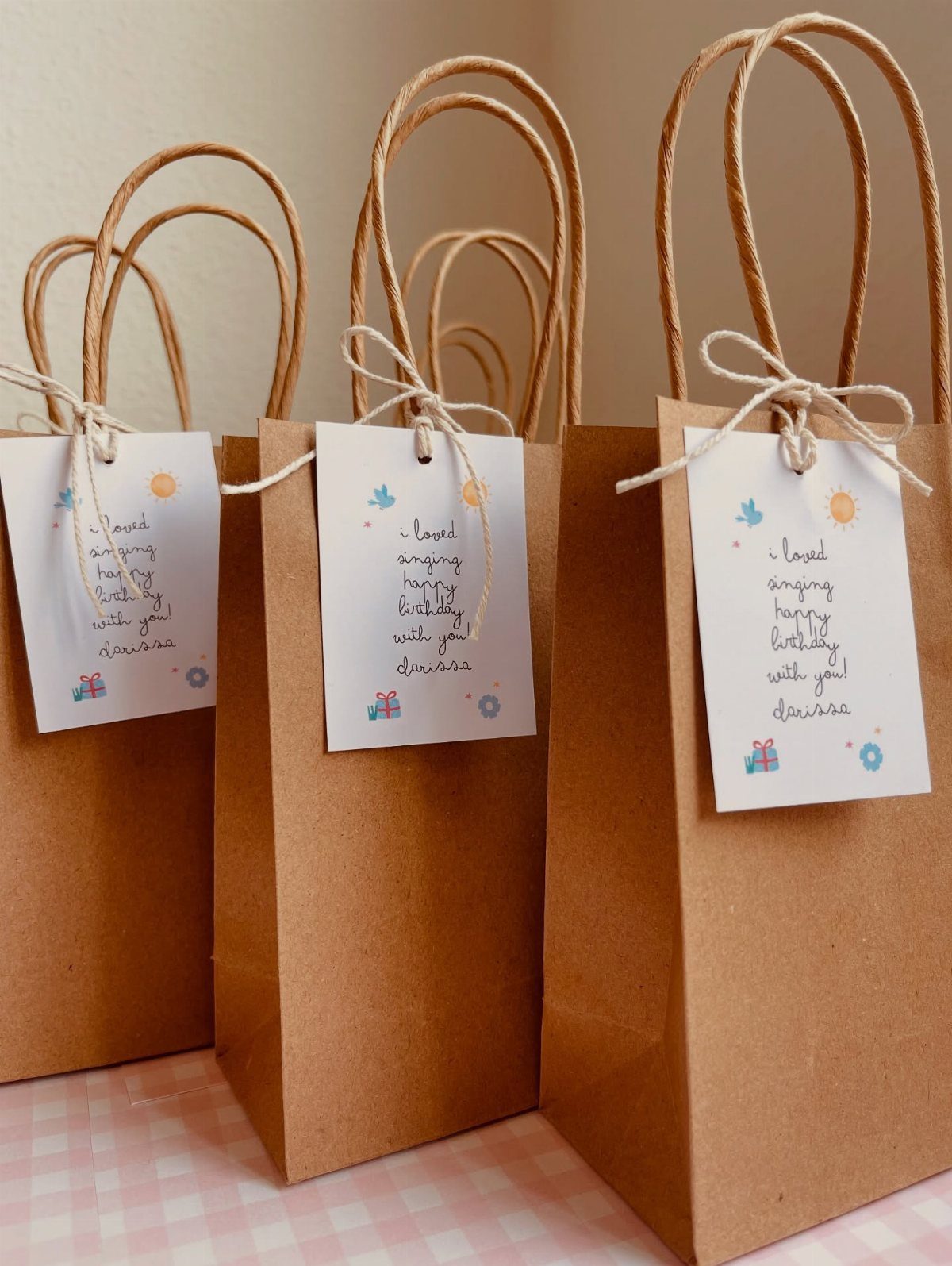 Brown kraft paper gift bags with white handwritten tags tied with string.