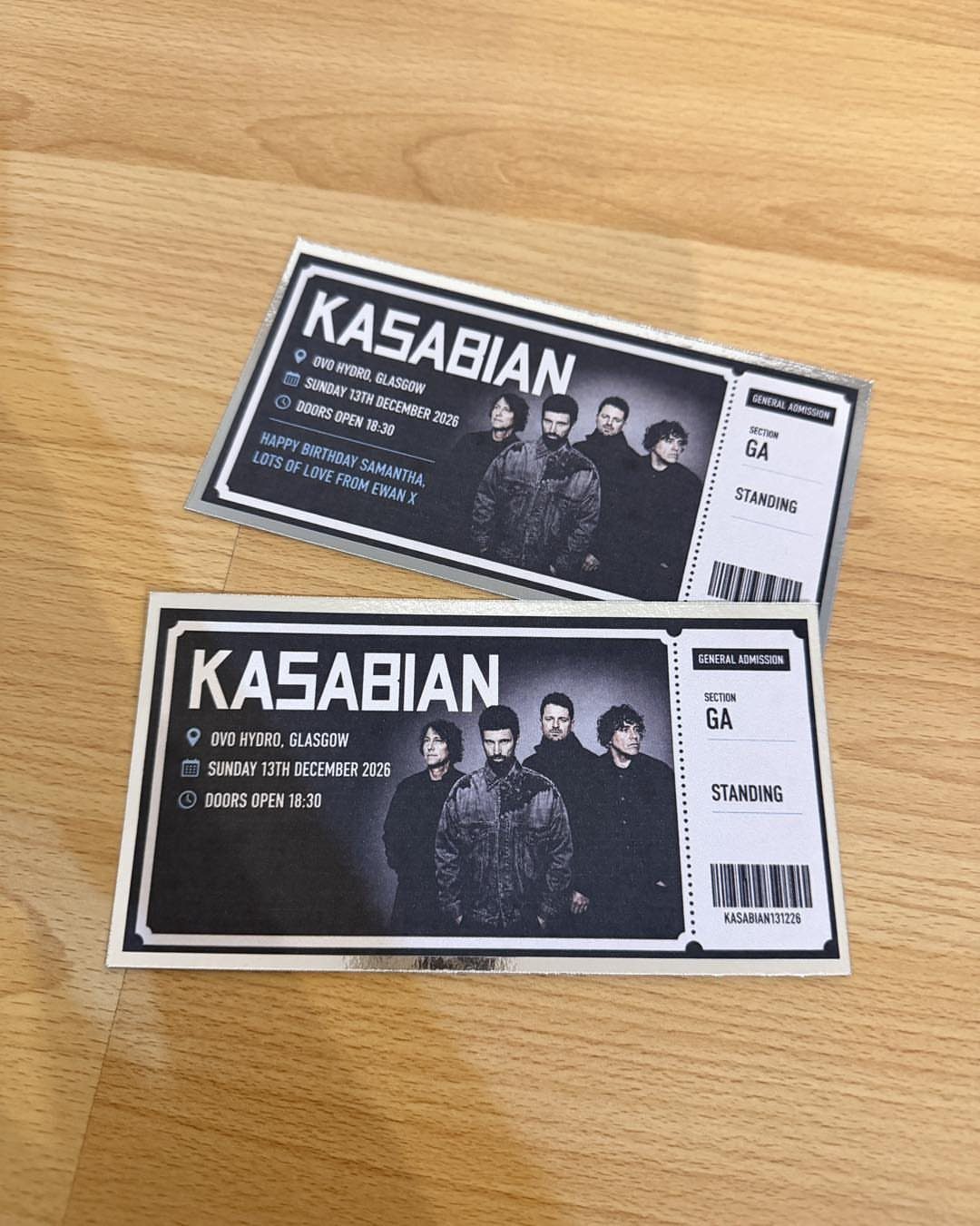 Two black and white Kasabian concert tickets resting on a light wooden table.