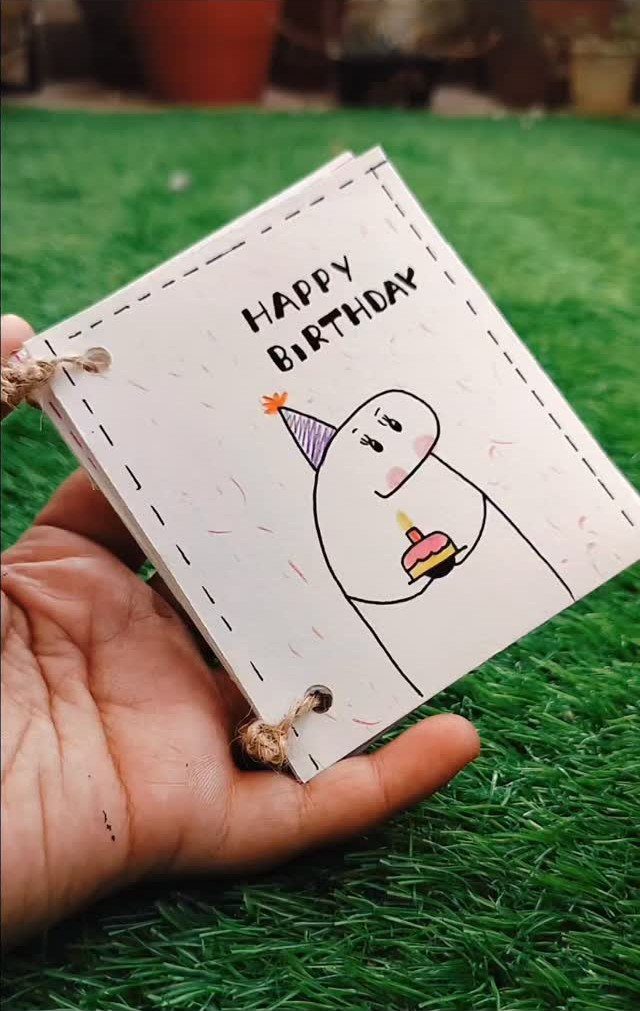 Handmade birthday notebook with a cute character drawing held over green grass