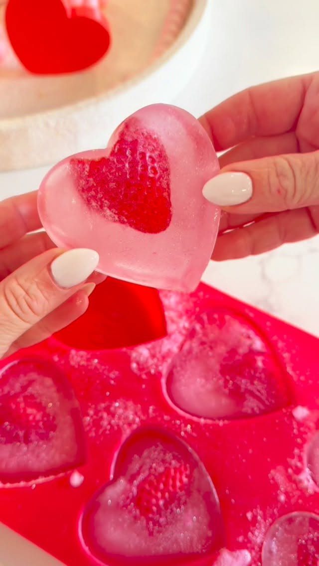 Heart-shaped ice cubes with red centers held over a red silicone mold.