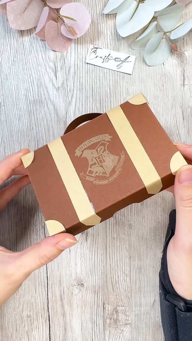 Brown suitcase-style gift box with Hogwarts crest held by two hands.