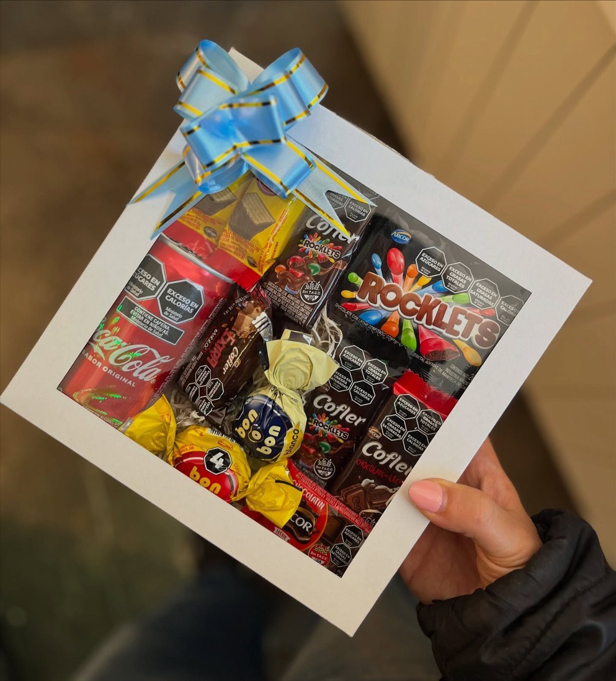 White gift box filled with assorted candies and chocolates topped with a blue bow.