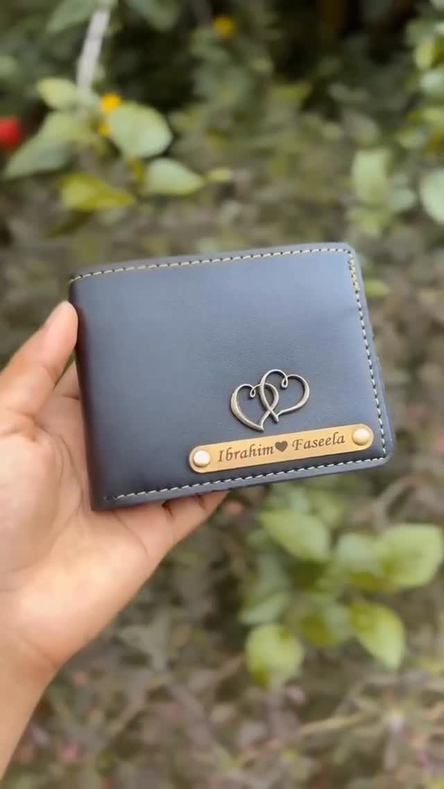 Dark blue leather wallet with gold heart and personalized nameplate held in hand.