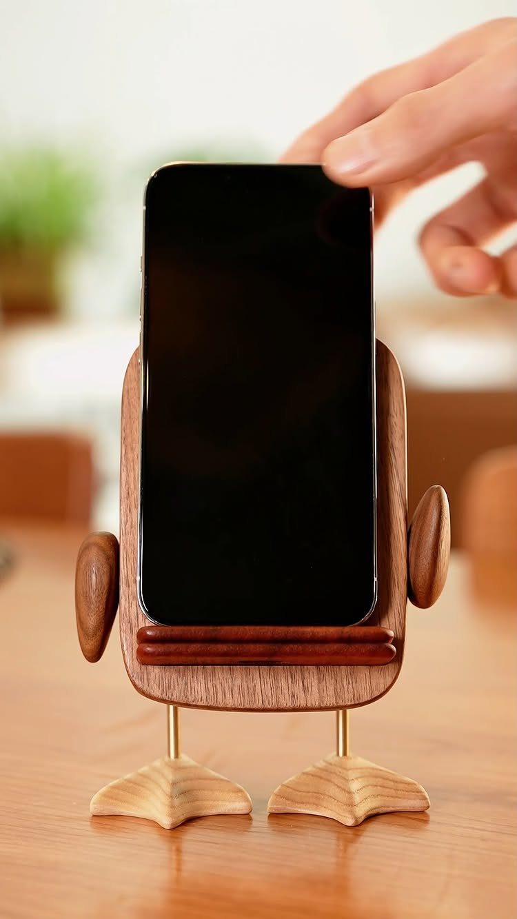 Wooden robot smartphone stand holding a black phone on a wooden table