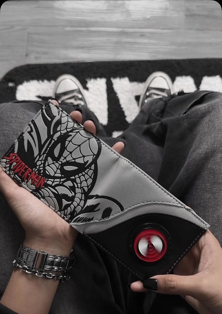Spider-Man themed wallet held by a person wearing a silver watch and sneakers.