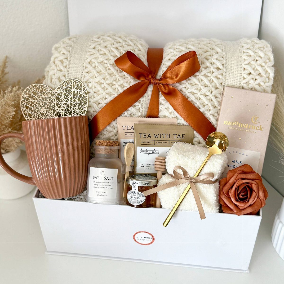 Gift box with brown mug, tea bags, honey, and a white knit blanket.
