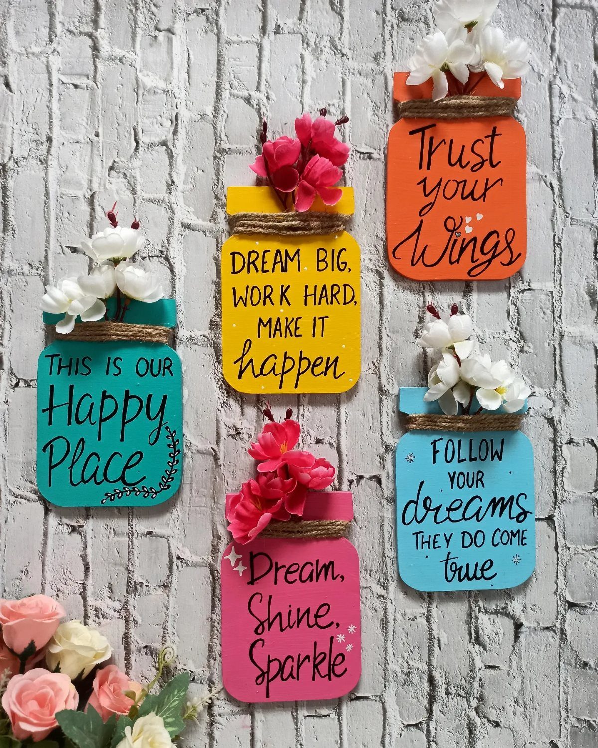 Colorful jar-shaped wooden plaques with motivational quotes and flowers on a brick wall