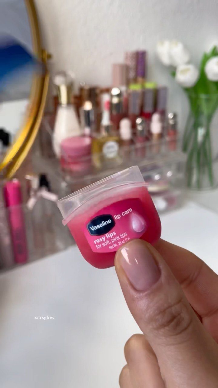 Pink Vaseline lip care jar held by a hand against a makeup background.