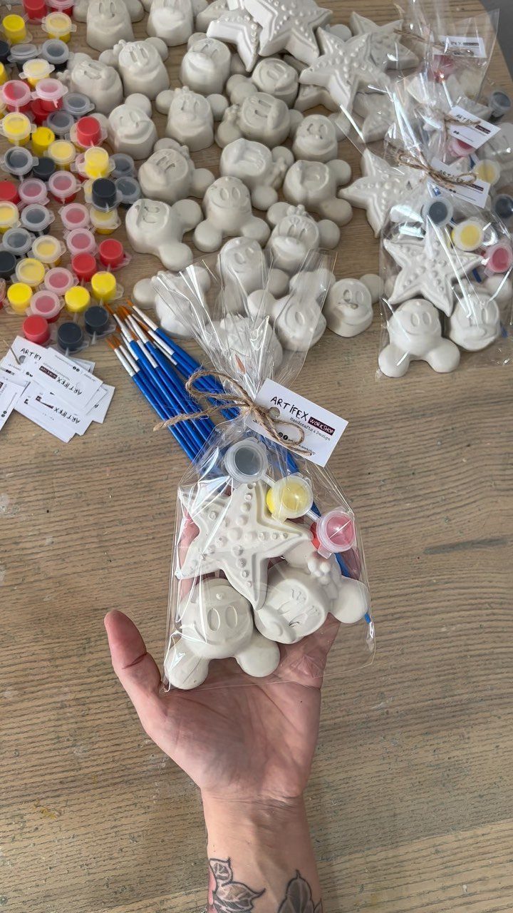Hand holding a DIY painting kit with plaster shapes, brushes, and paints.
