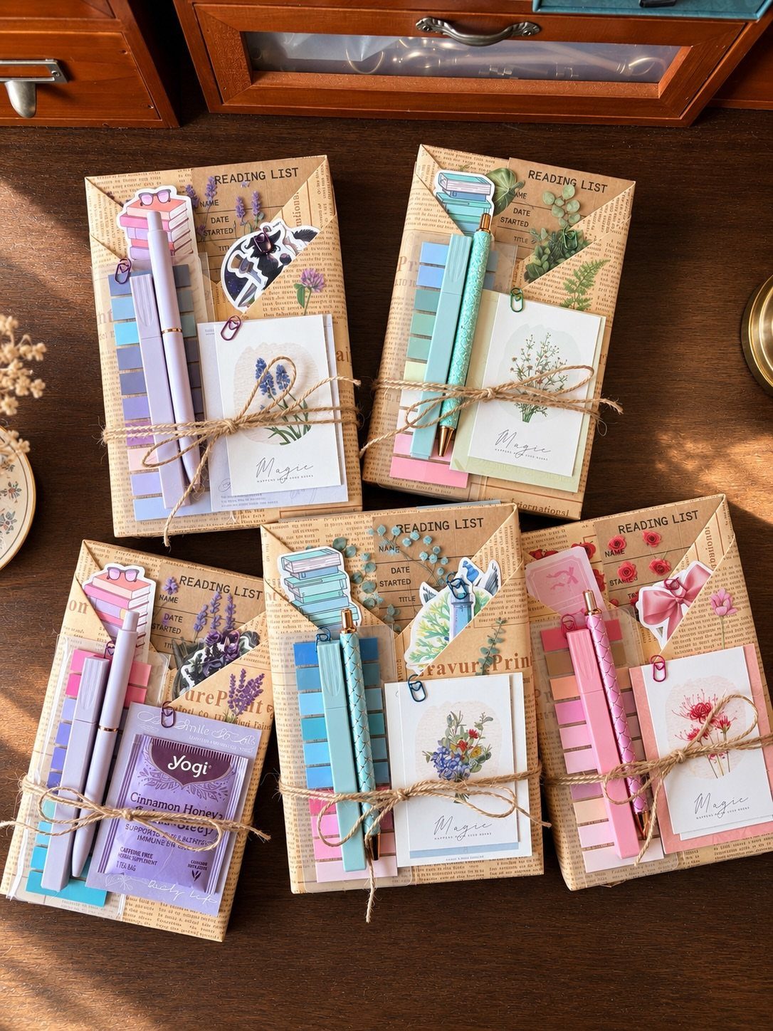 Four curated stationery gift sets with notebooks, pens, and tea on wood.