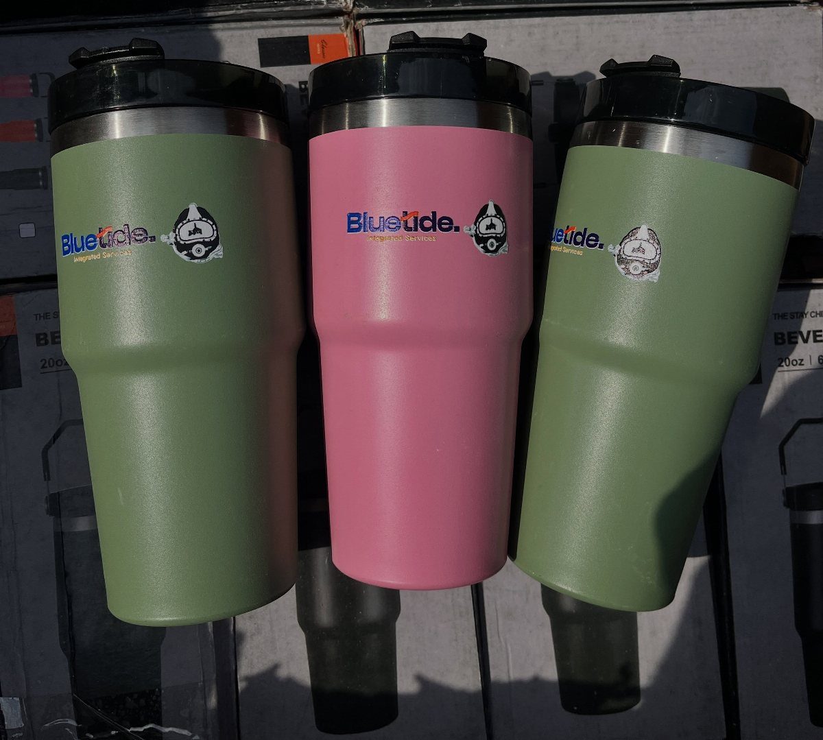 Three insulated travel mugs in pink and olive green with company logos.