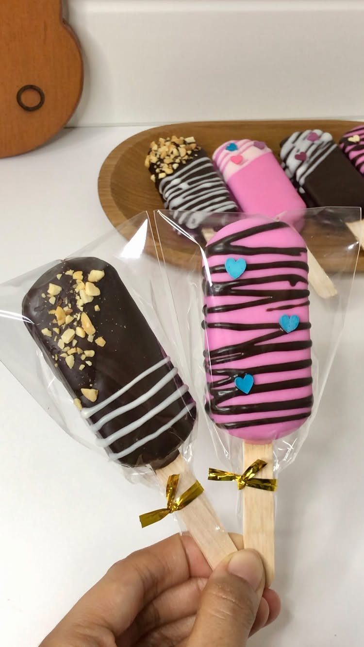 Popsicle-shaped chocolate treats wrapped in plastic with gold ribbons held by a hand.