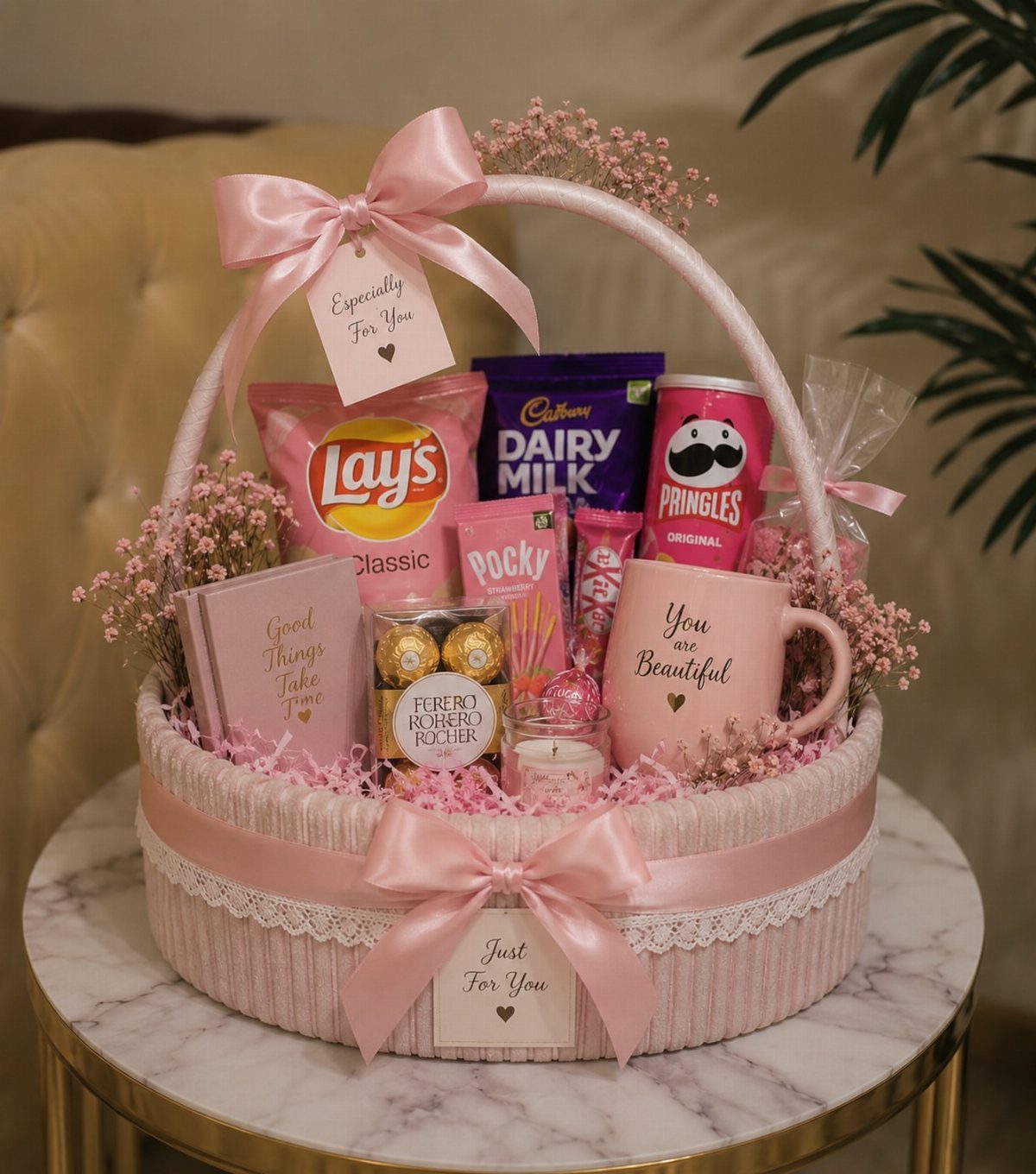 Pink gift basket filled with snacks, a mug, and a notebook with ribbons.