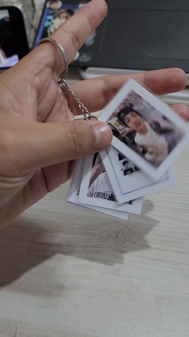 Hand holding a handmade keychain featuring small polaroid photos of a person.