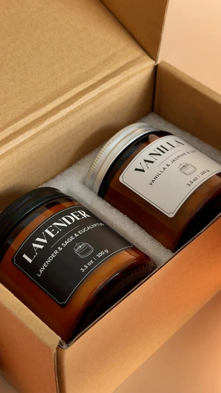 Two amber glass scented candles in a cardboard shipping box with foam padding.