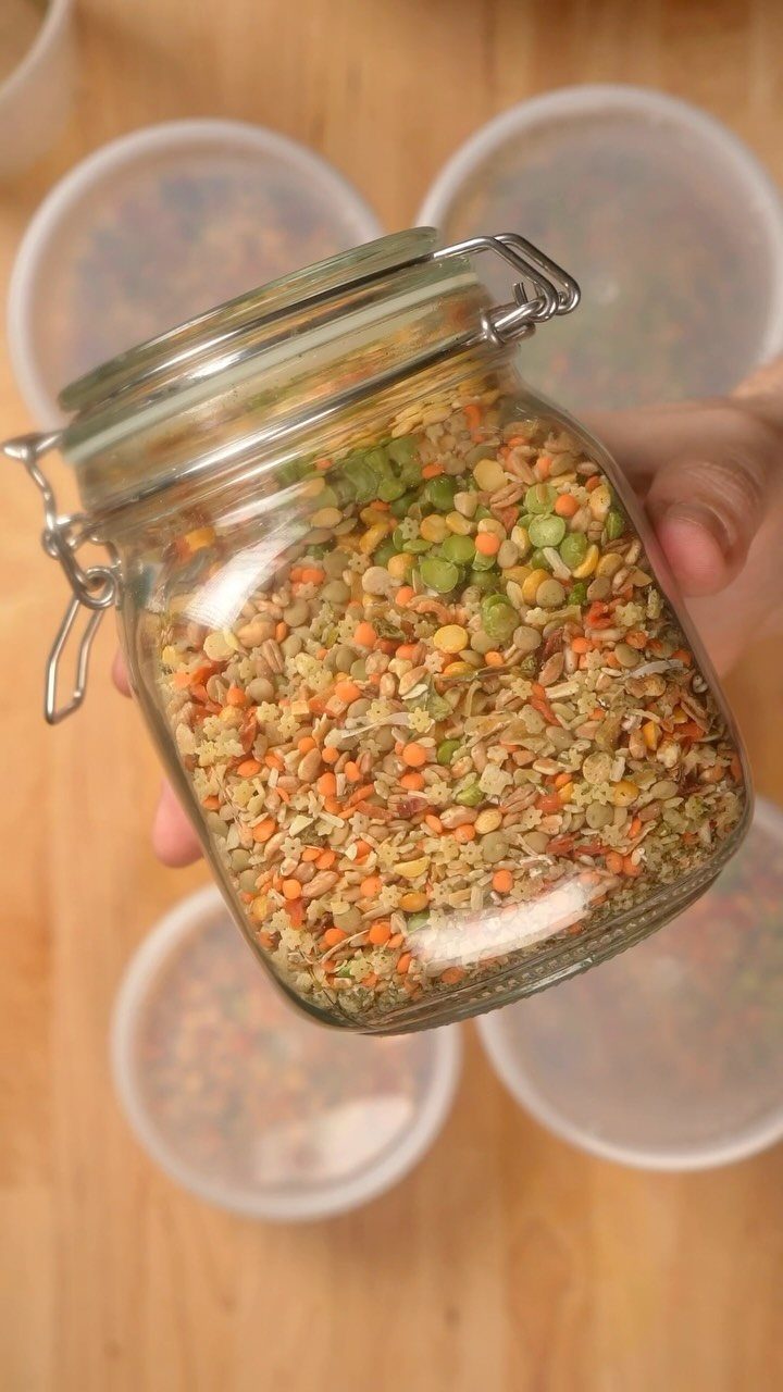 Glass jar filled with dried soup mix held over a wooden table
