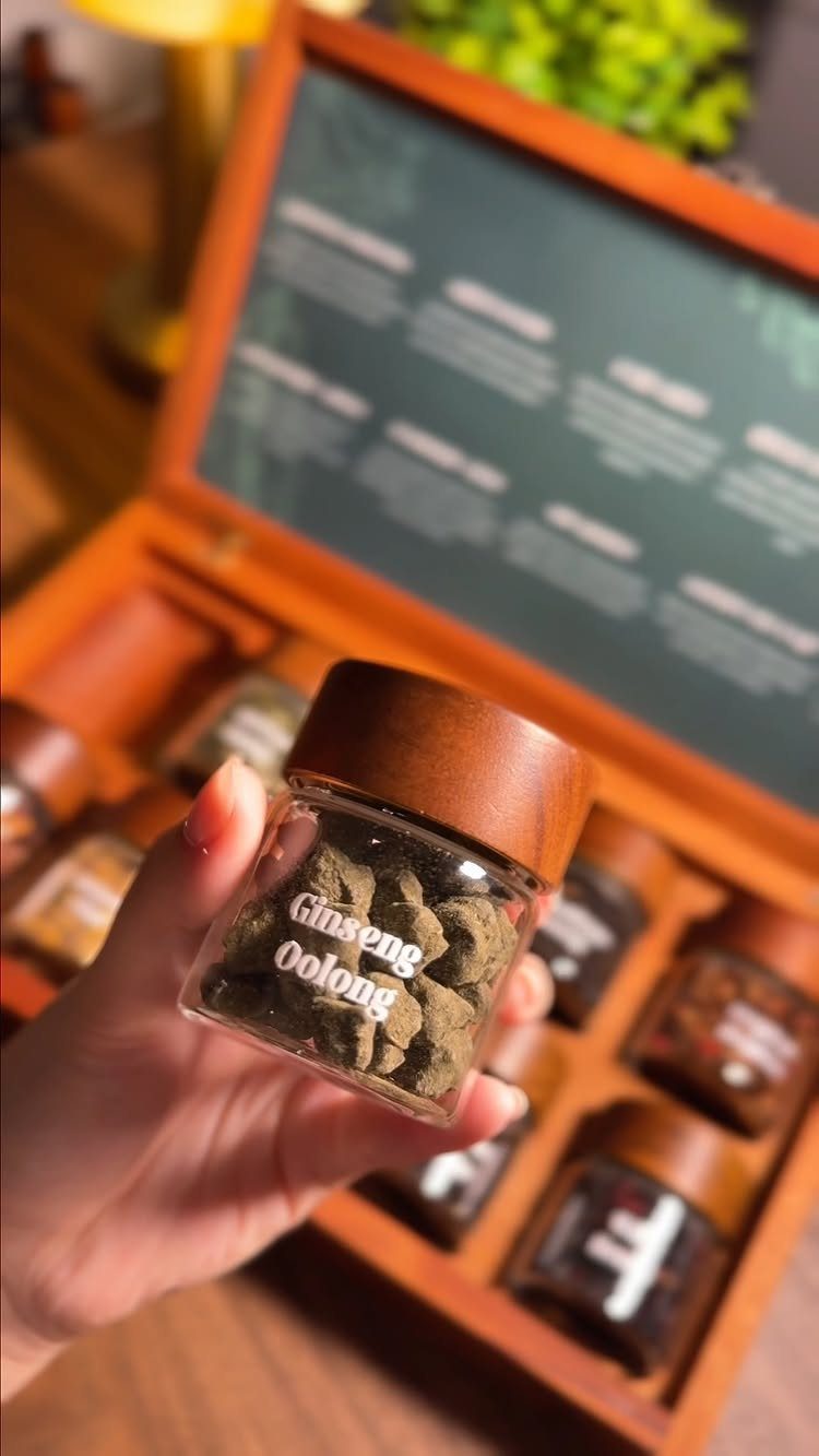 Hand holding a small jar of oolong tea from a wooden tea sampler set