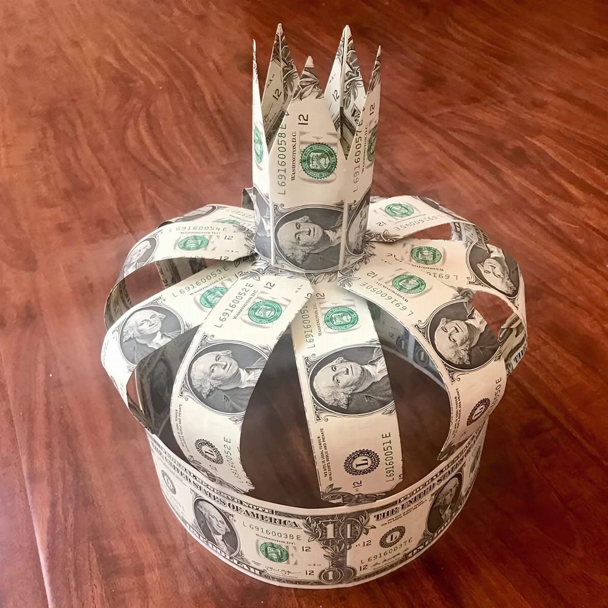 Crown made from folded ten-dollar bills resting on a brown wooden table.