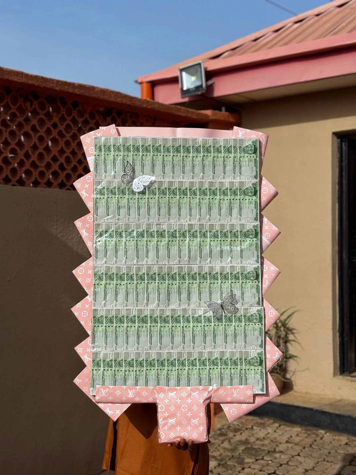 Rolled green banknotes arranged in a grid with a pink fabric border and butterflies.